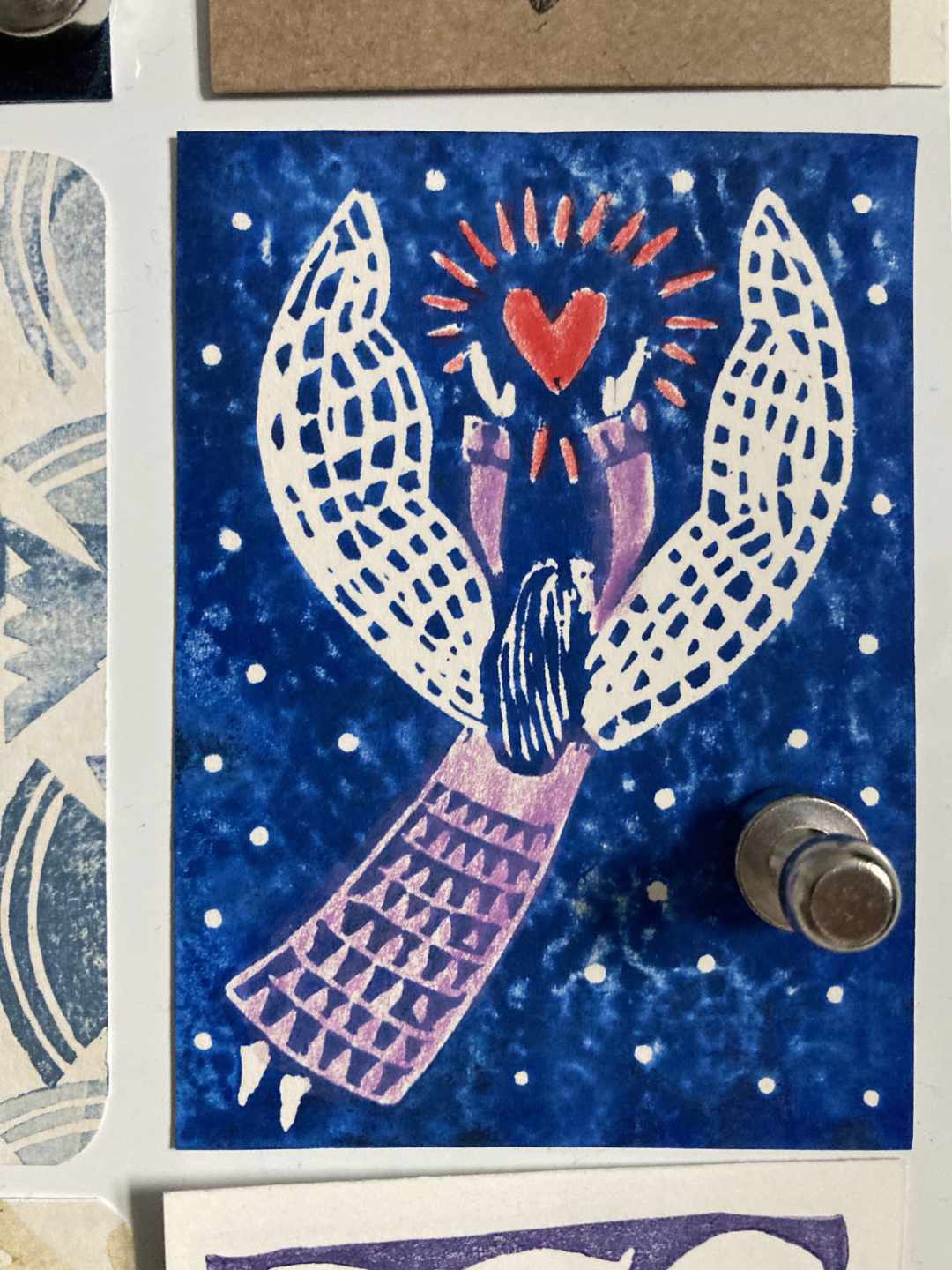 Eine ATC Karte mit Engelsdruck von Therese Olivier. Blau im Linoldruck, koloriert mit Buntstift in Rot und Rosa.